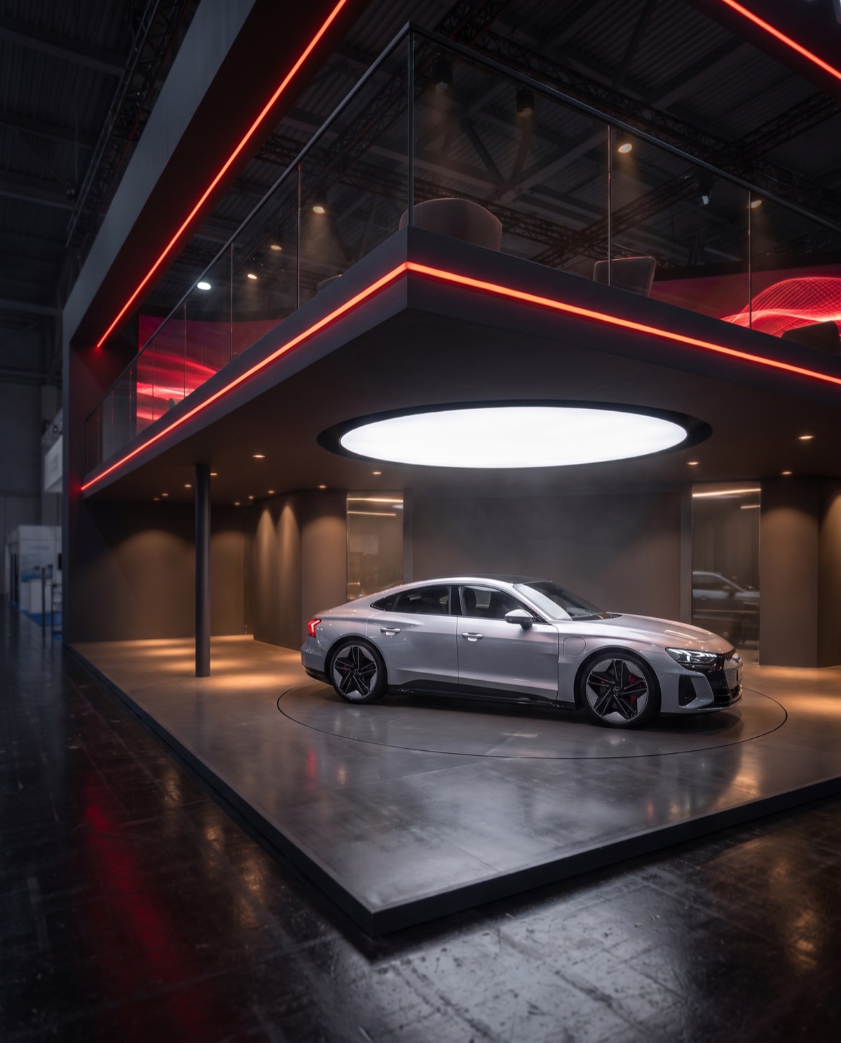 Close-up 3D render of a silver electric coupe on a turntable under a two-storey stand with red light lines